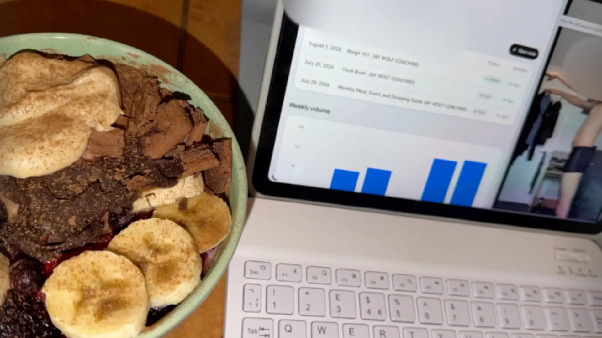 An iPad on a keyboard showing coaching documents and a weekly volume chart, with a video call open beside them and breakfast in front