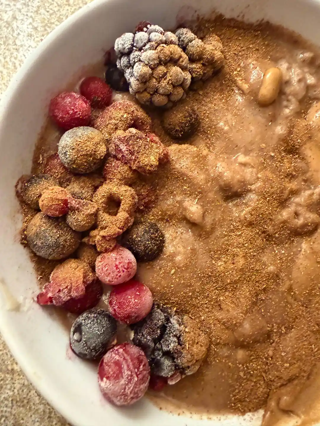 A bowl of porridge swirled with peanut butter and dusted with cinnamon, topped with frozen raspberries, blackberries and blueberries